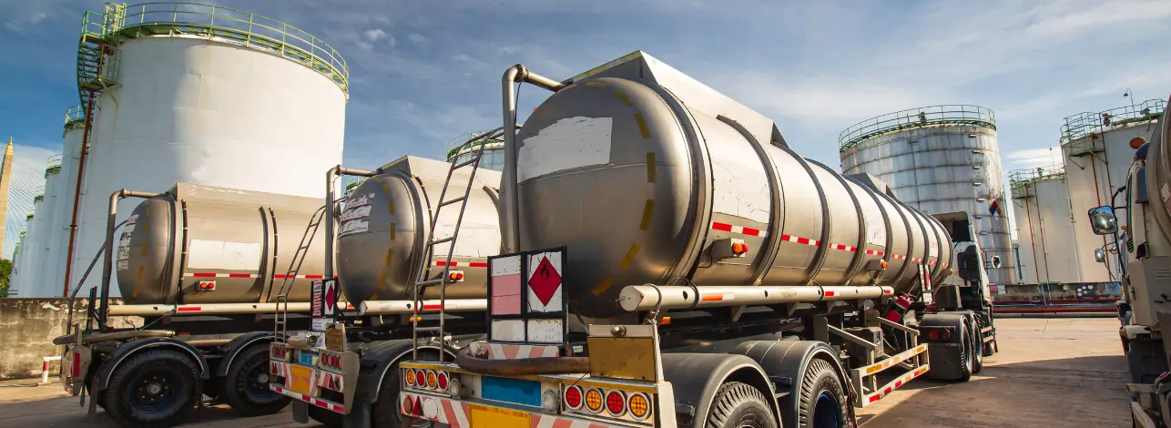 Fleet of tanker trucks at an industrial facility with large storage tanks in the background.