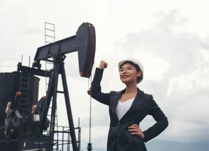 Engineer in black suit and white hard hat standing with raised fist in front of an oil rig, representing oilfield efficiency and downtime reduction.