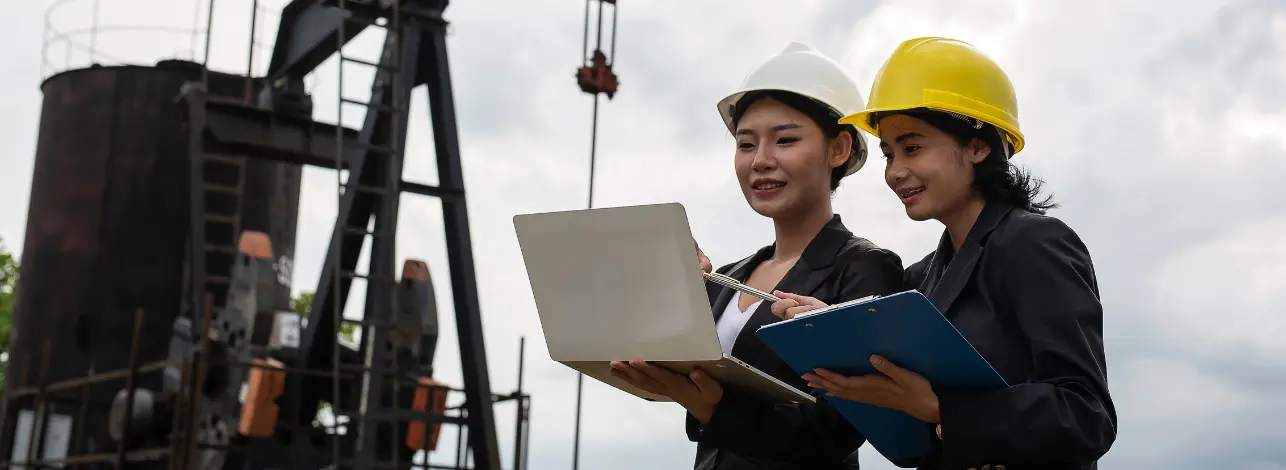 Two engineers with laptop and clipboard monitoring oil rig operations, representing data-driven chemical solutions to reduce oilfield downtime.