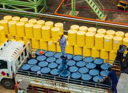 Workers managing blue and yellow barrels at a Houston transloading site with industrial piping and metal structures.