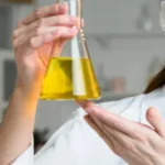 Laboratory technician holding a conical flask with yellow liquid, illustrating crosslinker selection in oilfield operations,