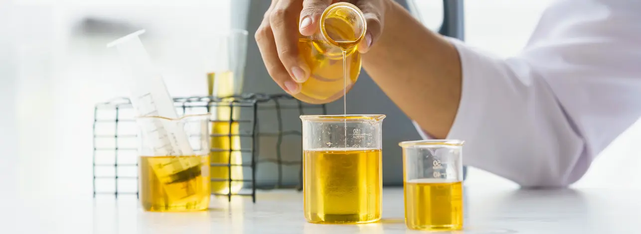 Lab technician pouring yellow chemical formulation into a beaker, with graduated cylinders on the table—demonstrating oilfield-specific chemical testing.