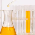 Biocide chemical being dispensed into flask for oilfield microbial control with test tubes in background.