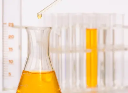 Biocide chemical being dispensed into flask for oilfield microbial control with test tubes in background.