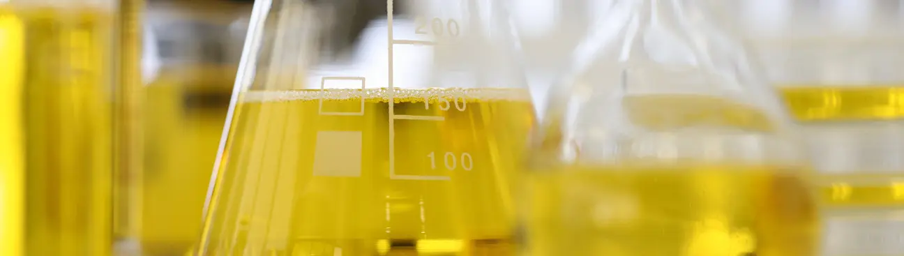 Laboratory flasks with yellow biocide solution for oilfield microbial control and corrosion prevention