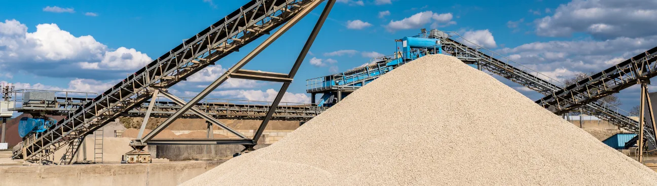 Industrial frac sand processing site with conveyor belts and metal structures under a blue sky.