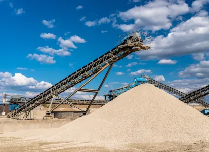 ndustrial site with a large pile of frac sand and conveyor belts under a blue sky with clouds.