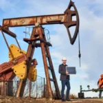Hydraulic fracturing site with oil pump jack, worker holding solar panel, and another operating equipment