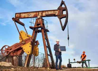 Hydraulic fracturing site with oil pump jack, worker holding solar panel, and another operating equipment